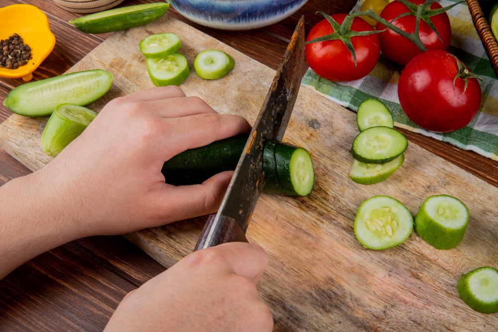 Side view of hands cutting cucumber with a knife on a cutting board